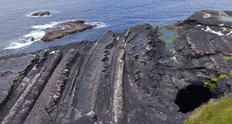 Des formations rocheuses sombres et dentelées avec des mares de marée rencontrant les eaux bleu profond de l'Atlantique.