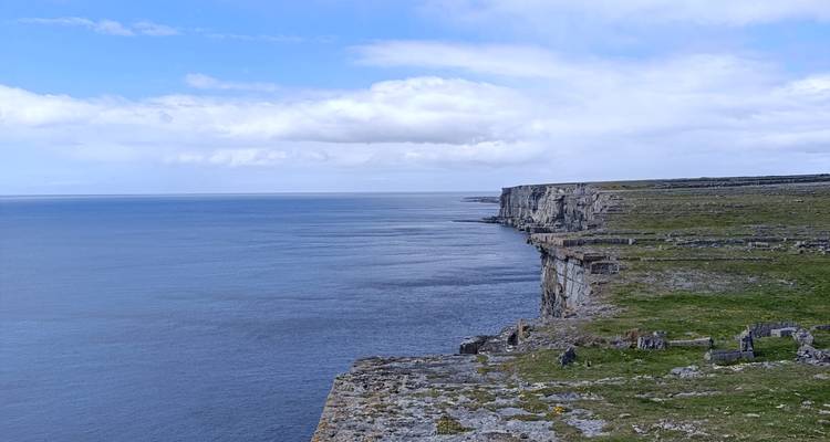 Des falaises côtières abruptes qui plongent vers une mer calme avec des ruines de pierre en bordure d'une pelouse.