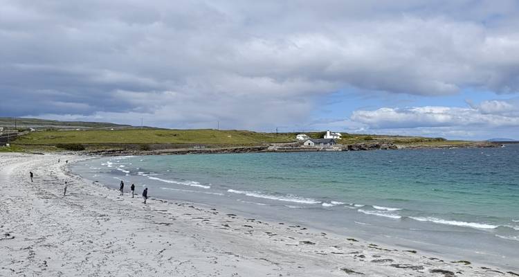 Plage de sable blanc avec eau turquoise et petite chapelle sous un ciel dramatique.