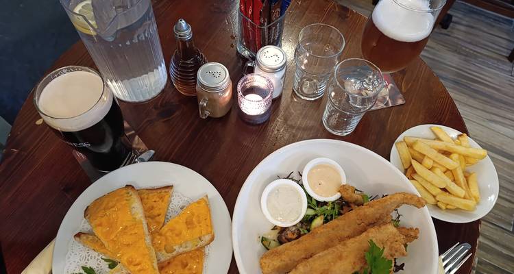 Table de pub garnie de poisson frit, tartines de fromage, frites, pintes et bougies.