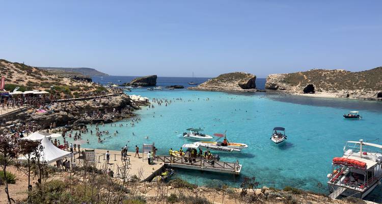 Busy Blue Lagoon with turquoise water, swimmers, rocky shore and anchored boats.