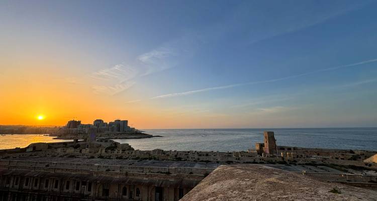 Golden sunset over coastal ruins and calm Mediterranean waters.