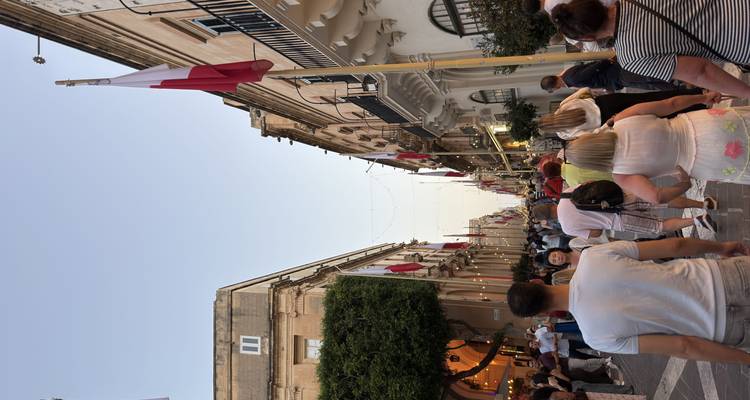 Crowded pedestrian street lined with Maltese flags during a festive evening.