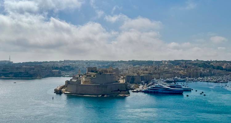 Panoramic view of Fort St Angelo and a marina full of yachts in bright blue water.