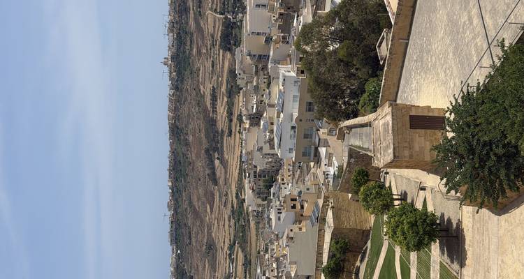 Elevated view over a terraced townscape and arid countryside of Gozo.