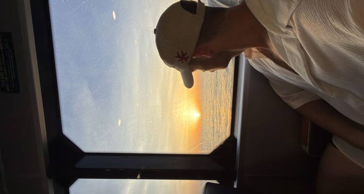 Traveller on a ferry gazing at a vibrant sunset over the sea through a window.