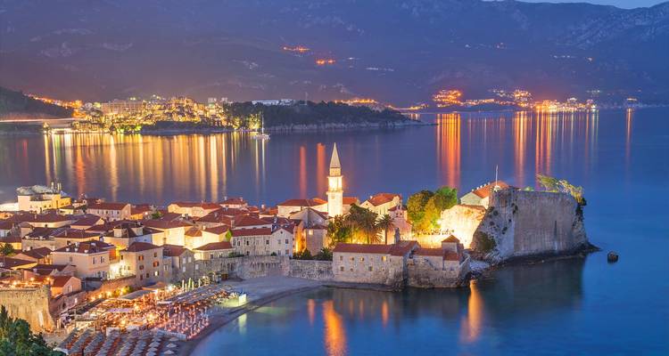 Panorama nocturne de la Vieille Ville de Budva et de la forteresse illuminée se reflétant sur la mer Adriatique.