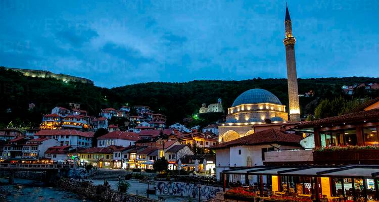 Scène en soirée de Prizren avec la Mosquée Sinan Pasha illuminée et les maisons sur les pentes.
