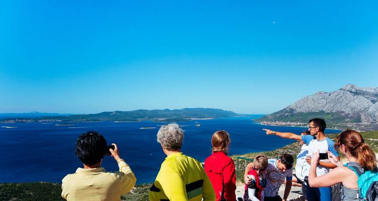 Les visiteurs admirent et photographient l'Adriatique bleu profond et les îles dispersées depuis un belvédère élevé.