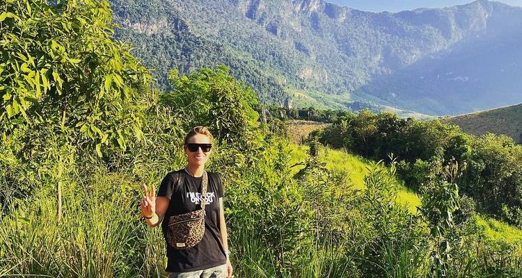 Traveller posing with peace sign amid green hills and distant cliffs on a sunny day.