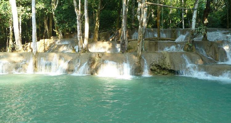 Turquoise tiers of a jungle waterfall cascade into a clear pool surrounded by trees.