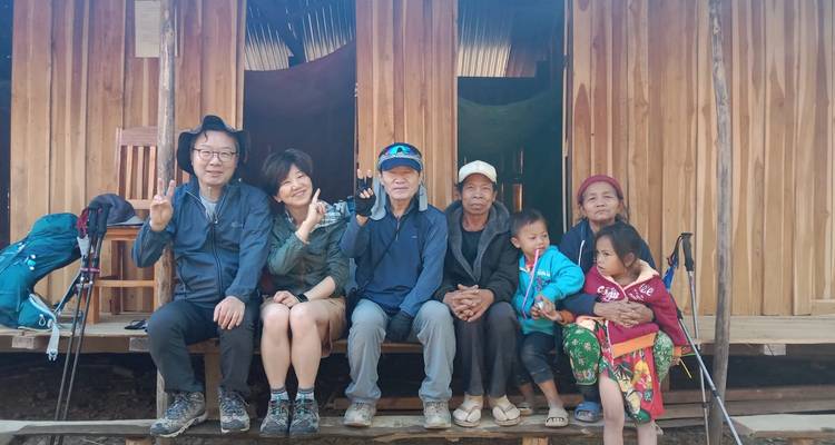 Travellers and local villagers sit together on a wooden porch, smiling and gesturing peace signs.