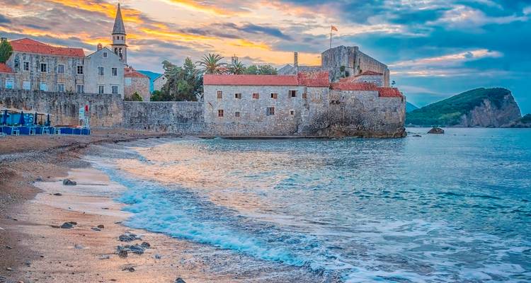 Stone walls of Budva Old Town on a tranquil beach at sunset with pastel clouds over the Adriatic