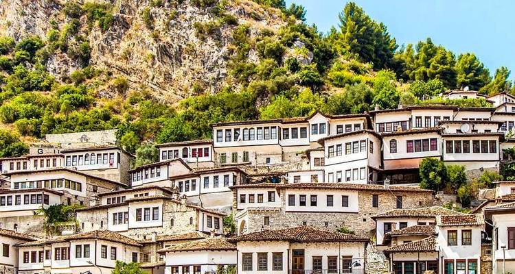 Traditional white Ottoman houses stacked on a rocky hillside covered with greenery under a bright sky