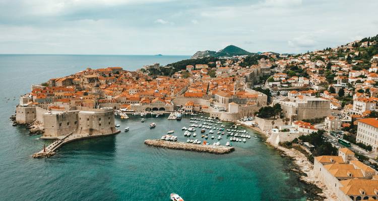 Drone view of Dubrovnik’s walled old city jutting into turquoise waters with yachts docked in the harbour