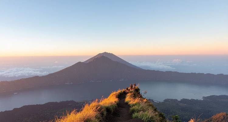 Vue du lever de soleil depuis la crête volcanique surplombant le Mont Batur et son lac de cratère avec des randonneurs sur le sentier.