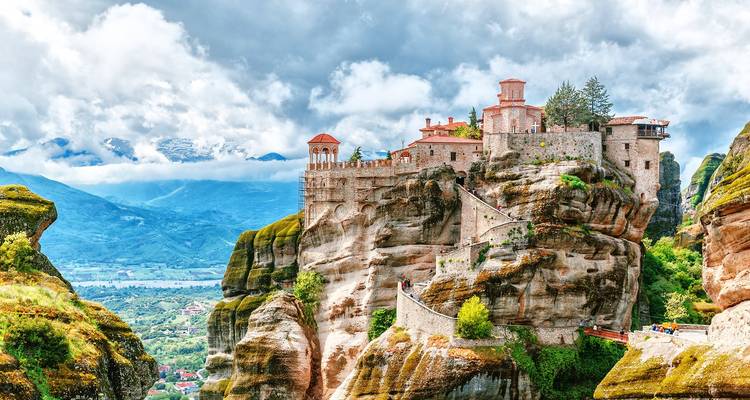 Monasterio dramático encaramado en lo alto de enormes pilares de roca en Meteora con nubes y valles abajo