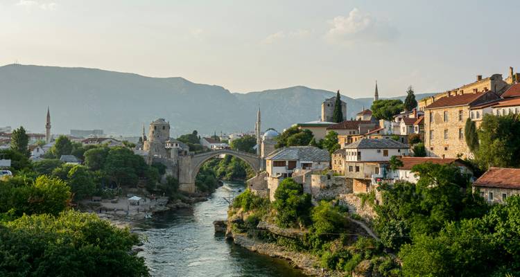 Puente de piedra histórico arqueado sobre el río esmeralda en Mostar con minaretes y montañas al fondo