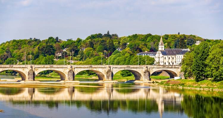 Stone arch bridge spanning the Loire River with church and lush hillside reflected in calm water.