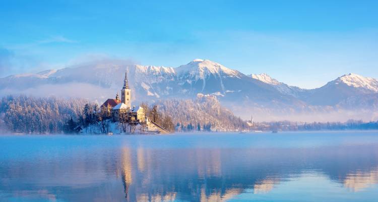 Montagnes enneigées se reflétant dans la brume hivernale tranquille au-dessus du lac de Bled et de l'église insulaire