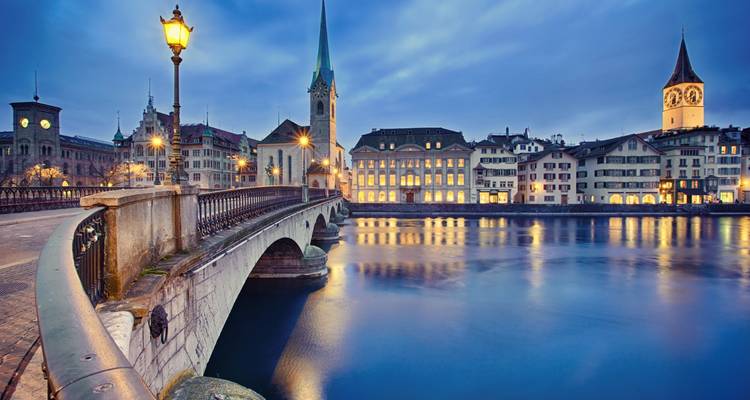 Twilight scene of Zurich with historic bridges, Fraumünster church spire and calm reflections in the Limmat River.