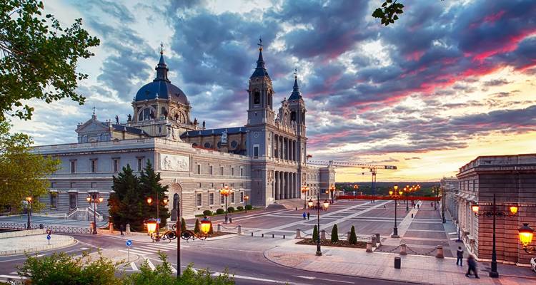 Kathedrale Almudena in Madrid mit dramatischen Sonnenuntergangswolken und klassischen Straßenlaternen im Vordergrund