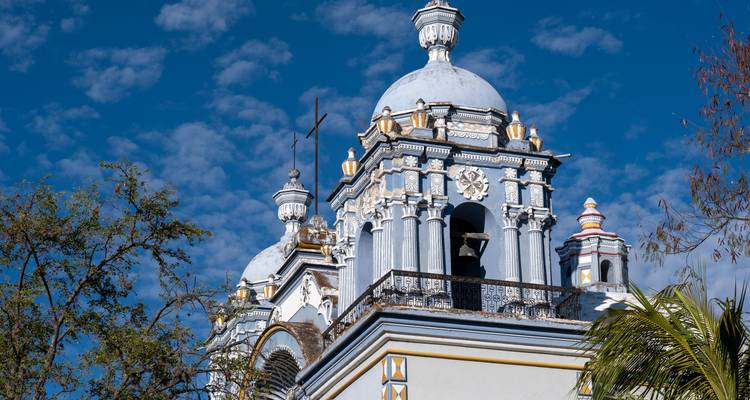 Dôme d'église de style baroque aux détails ornés se détachant sur un ciel bleu aux motifs.