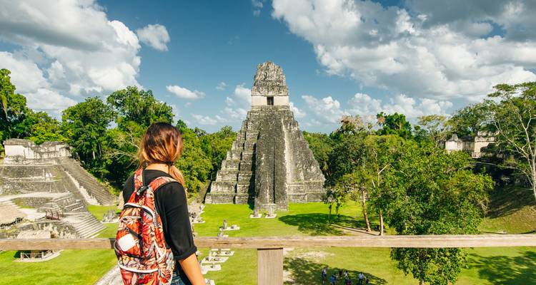 Un visiteur portant un sac à dos à motifs surplombe le majestueux Temple I à Tikal, entouré par la jungle.