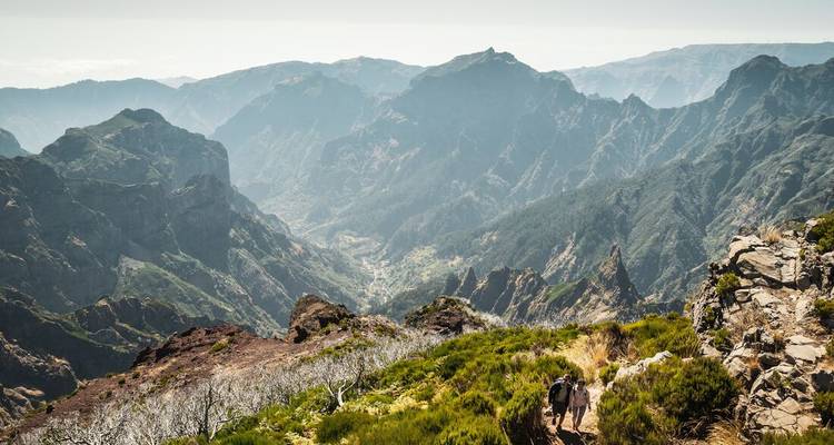Sweeping mountain valley view on Madeira with two hikers walking along a rugged ridge trail.