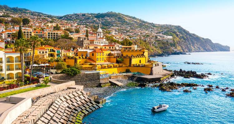 Colorful coastal cityscape of Funchal with yellow fort, terraced hills and blue Atlantic waters.