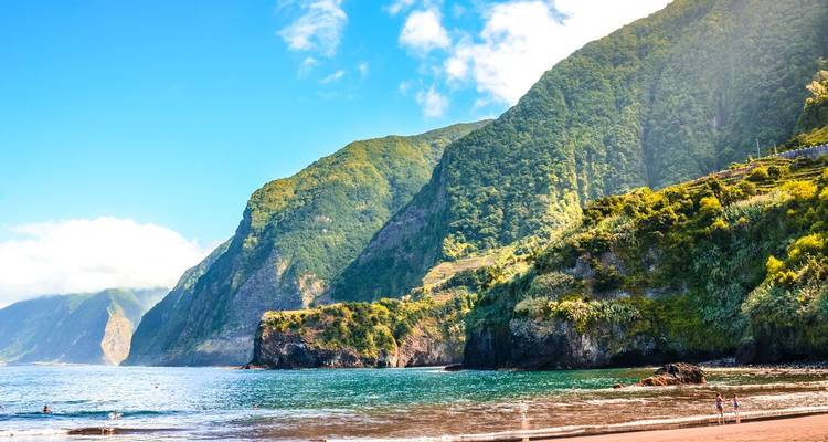 Sandy beach backed by towering green cliffs and clear turquoise sea on Madeira’s north coast.