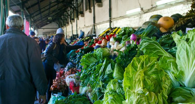 Marché couvert animé avec des acheteurs parcourant des tas vibrants de légumes feuillus frais.