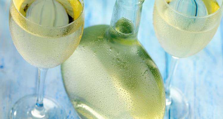 Deux verres refroidis et une bouteille de vin blanc givré sur une surface en bois bleu.