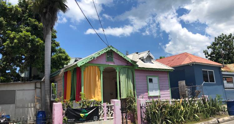 Maison caribéenne en bois coloré aux murs pastel et aux tissus drapés, située sous un ciel bleu éclatant.