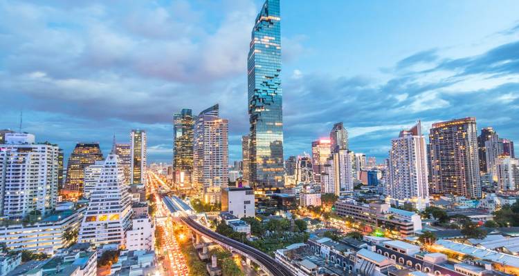 Twilight cityscape of Bangkok’s skyline featuring the pixelated MahaNakhon tower and light-trailed traffic below.