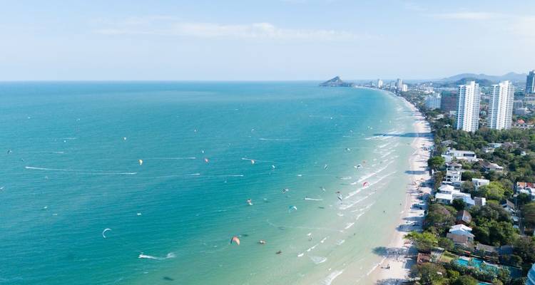 Drone shot of Hua Hin’s extensive beachfront with turquoise sea and scattered kite surfers.