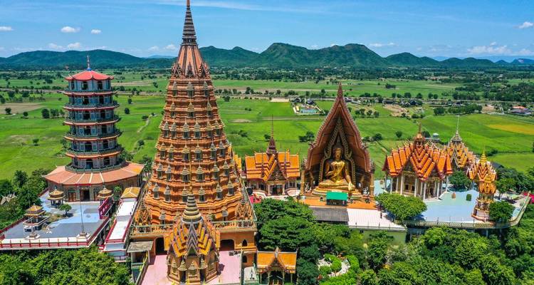 Aerial panorama of Wat Tham Sua complex with ornate orange towers and giant Buddha statue amid green fields.