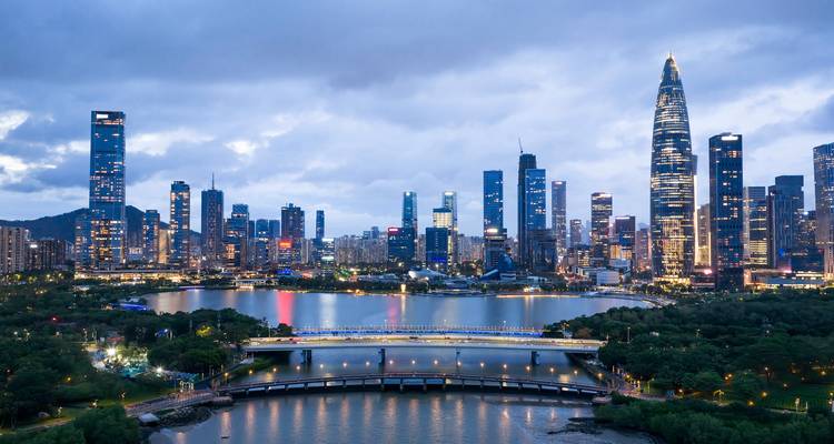 Panoramablick bei Einbruch der Dunkelheit auf Shenzhens futuristischen Horizont, der sich in einem Stadtsee spiegelt, mit beleuchteten Bruecken.