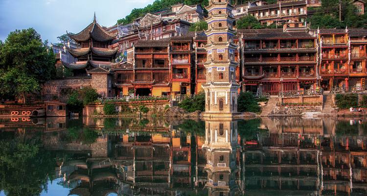 Traditionelle hölzerne Flussuferbauten und Pagodentürme, die sich in ruhigen Gewässern des historischen Fenghuang Ancient Town widerspiegeln.