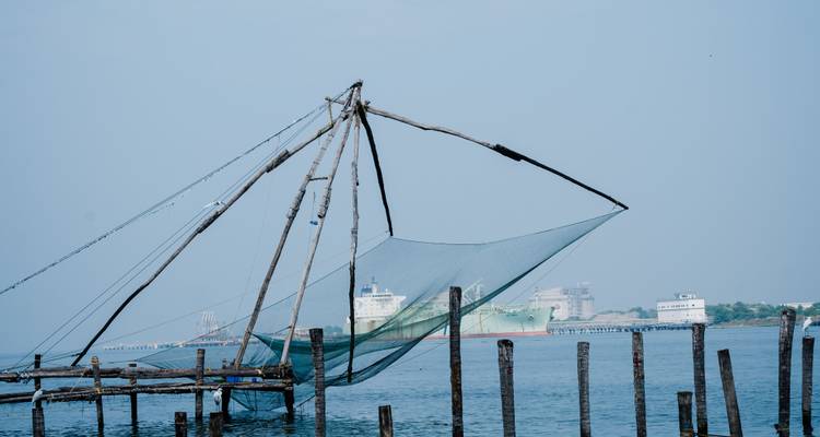 Traditionelle chinesische Fischereinetzstruktur erstreckt sich über ruhige Gewässer mit fernen Schiffen in der Nähe von Kochi.