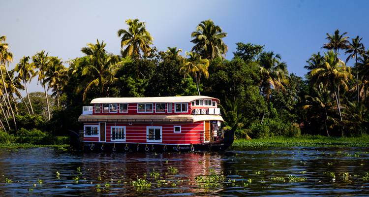 Das rote zweistöckige Hausboot aus Kerala gleitet entlang der spiegelnden Backwaters, die von üppigem Palmwald gesäumt sind.