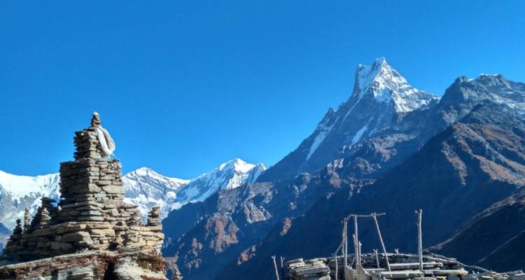 Cairn de pierre au premier plan avec un groupe de pics enneigés incluant le Machapuchhare sur un ciel bleu clair