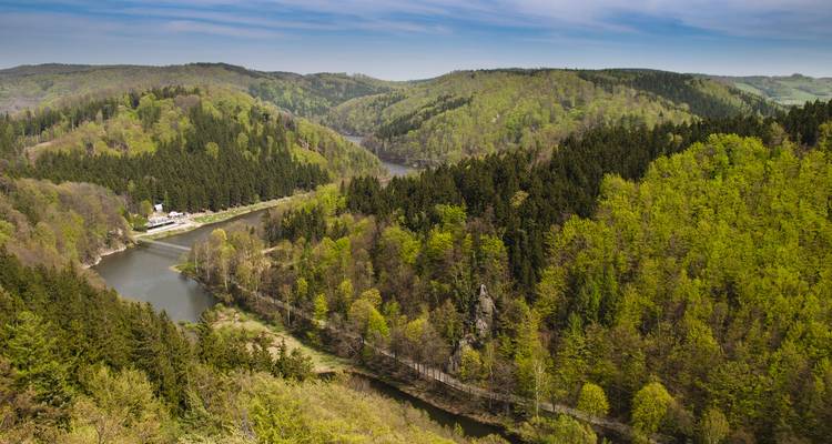 Forested hills and a winding reservoir nestled in the green countryside of the High Tatras region.