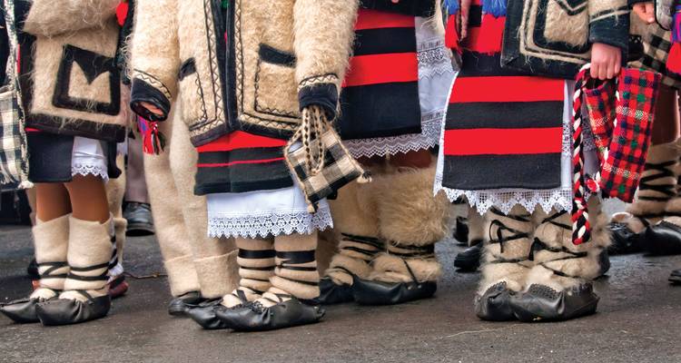 Lower legs of people wearing traditional woollen Romanian costumes with striped patterns and leather shoes.