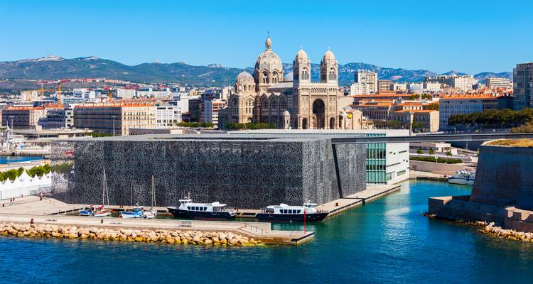 Das moderne MUCEM-Museum und die gestreifte Kathedrale von Marseille erheben sich neben dem türkisfarbenen Hafenwasser.
