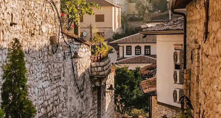 Rustic stone alley in an Albanian hill town with terracotta roofs and vines spilling over balconies.