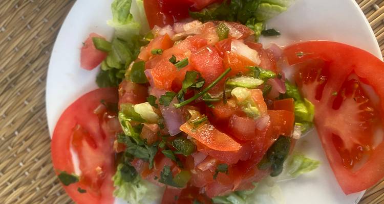 Salade de tomate fraîche et laitue disposée sur une assiette blanche à une table en plein air.