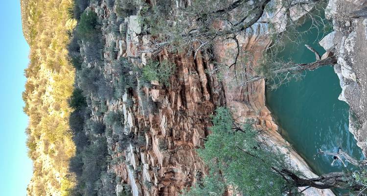 Canyon rocheux avec bassin naturel turquoise et végétation clairsemée sous un ciel dégagé.