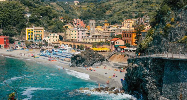 Sunny coastal town with pastel buildings, sandy beach, and turquoise Ligurian waters.
