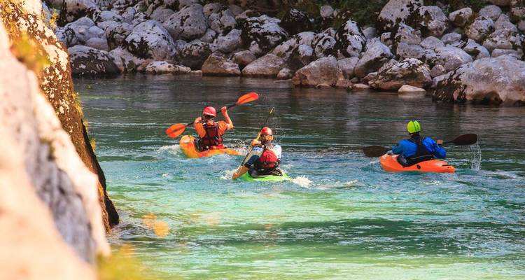 Kayakers paddle through clear turquoise river water framed by rocky banks.
